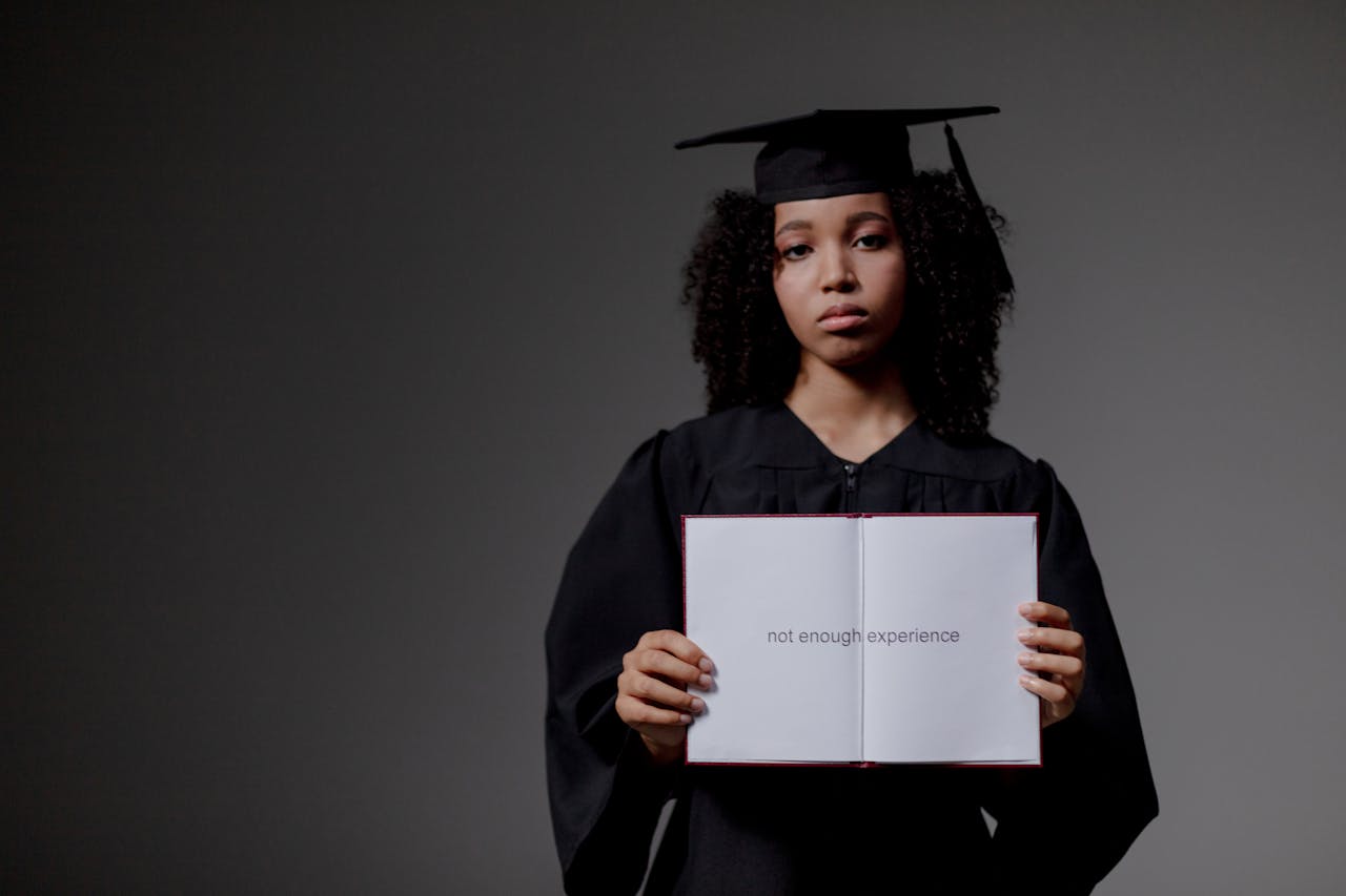 Young graduate holding a book with 'not enough experience' message, symbolizing job hunt difficulties.